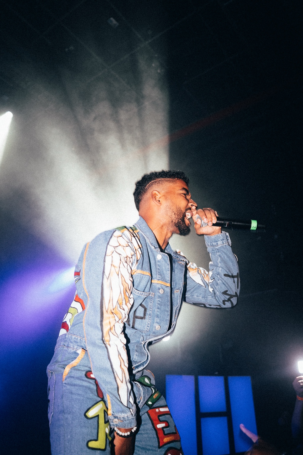APXO performing on stage into a microphone wearing a graphic denim jacket